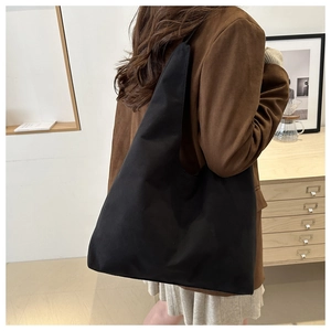 Close-up of a minimalist black matte tote bag worn on shoulder in an aesthetic cafe setting