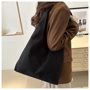 Side view of a large black canvas tote bag worn by a model in a minimalist setting