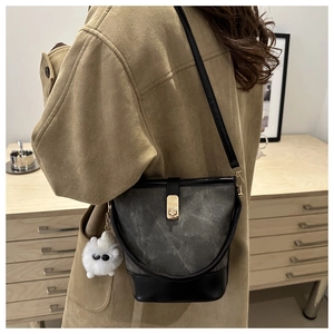 Detail of a contrasting bucket bag with gold clasp and fluffy white charm on handle