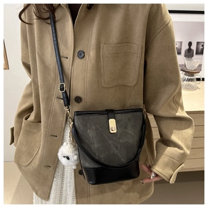 Detail of greyish-green bucket bag with black leather base and white plush charm