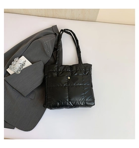 Macro detail of black quilted tote bag featuring a glossy nylon finish and gold snap pocket