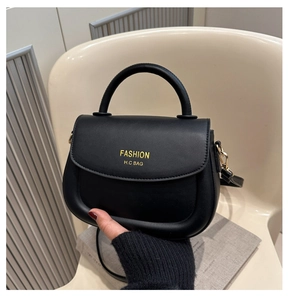 Detail of black leather saddle bag with gold FASHION lettering and detachable strap