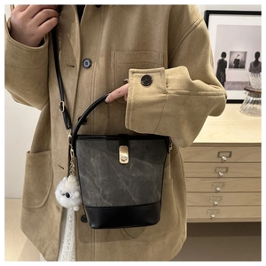 Detail of grey bucket bag with metal lock, plush charm, and black leather strap worn by model