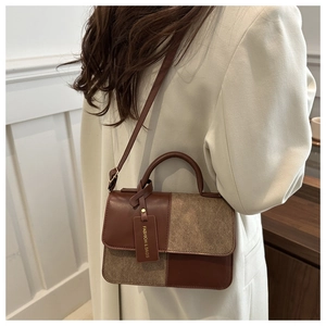 Detail of color-blocked crossbody bag in brown tones with handle and brand tag