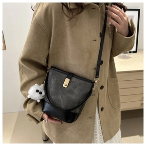 Detail of vintage textured crossbody bucket bag with golden buckle and white plush charm