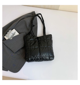 Detail of black quilted tote bag with reflective fabric and shoulder straps on white surface