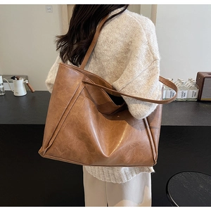 Side view of a large brown leather tote bag worn by a model in a cozy indoor setting