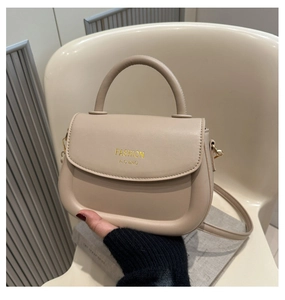Close-up of beige faux leather handbag with round handle and gold lettering on a chair
