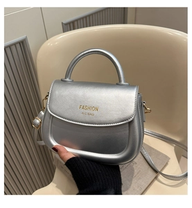 Macro shot of silver metallic saddle bag featuring gold fashion logo and top handle