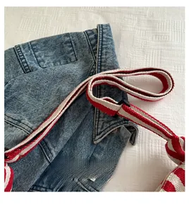 Close-up of blue denim bag featuring red and white striped strap and silver rivets