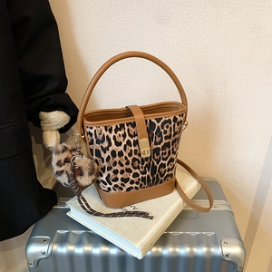 Leopard print bucket bag with brown leather handles and plush charm on white surface