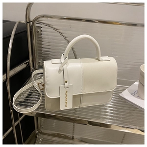 Detail of minimalist white leather handbag with stitched accents and fashion bag tag