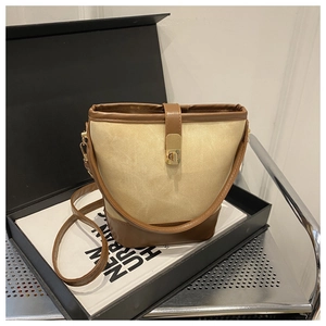 Detail of canvas bucket bag showing brown leather trim and golden metal turn-lock closure