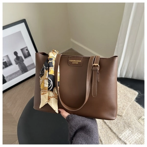 Close-up of brown leather tote bag with elegant silk scarf and gold brand plaque