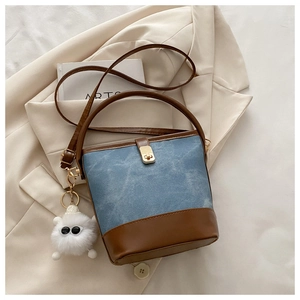 Detail of denim bucket bag with leather trim and a fluffy monster charm accessory