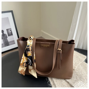Close-up of a dark brown leather tote bag with silk scarf and fashion logo engraving