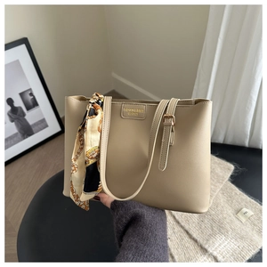 Macro view of beige leather tote bag featuring gold embossed text and decorative silk scarf