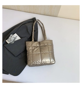 Close-up of champagne gold quilted puffer tote bag with metallic finish on white surface