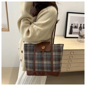 Detail of plaid tote bag showing grey pattern fabric and brown leather strap on shoulder