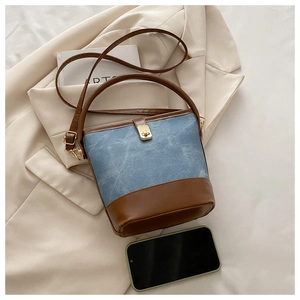 Detail of blue denim bucket bag with brown leather trim on beige blazer