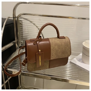 Close-up of color-block leather handbag with gold-tone fashion logo tag on metal shelf