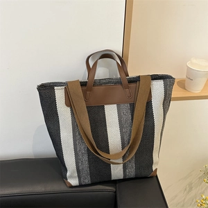 Detail of a striped tote bag with woven texture and brown leather corner protectors