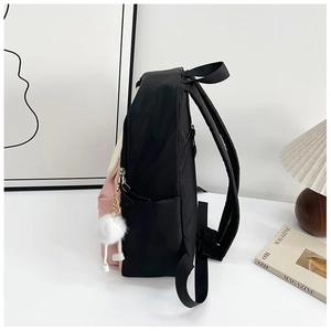 Side view of large color-block nylon backpack with pink panel and plush charm on desk
