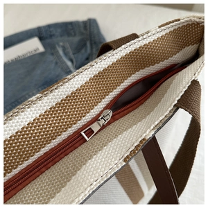 Close-up of the woven checkered tote bag featuring a brown zipper and metal hardware