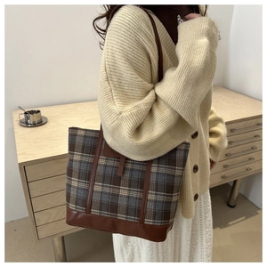 Dettaglio della borsa tote a scacchi con manici in pelle marrone su un maglione beige