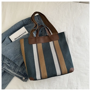 Detailed close-up of striped canvas tote bag with brown leather handles on white fabric