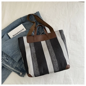 Detail of striped canvas tote bag with brown leather trim and handles on denim fabric
