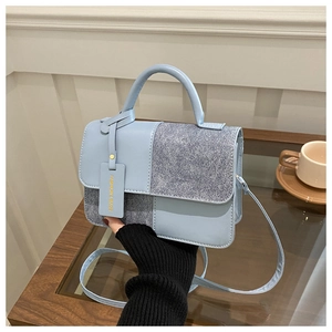 Close-up of light blue textured handbag with metal tag and detachable strap in a cafe setting