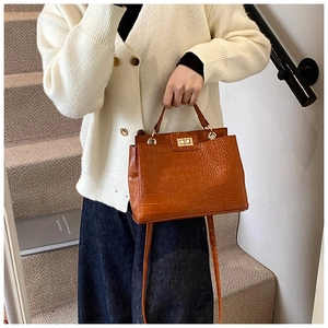Detail of brown crocodile embossed tote bag with gold twist lock and top handle grip