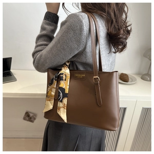 Brown leather tote bag detail with silk scarf and logo plaque in a modern office setting