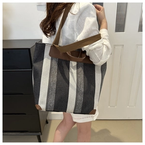 Close-up of striped canvas tote bag with brown leather trim worn by a model