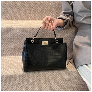 Détail d'un sac à main noir texture crocodile avec fermoir rotatif carré en métal doré