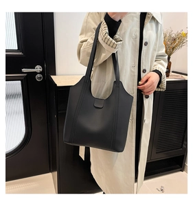 Detail of minimalist black tote bag with slender straps worn over a trench coat