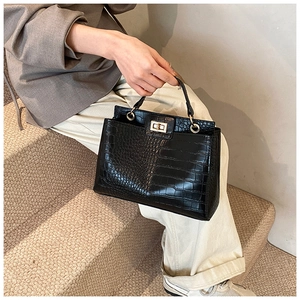 Détail du sac à main noir motif crocodile avec fermoir rotatif doré et anse ronde chic