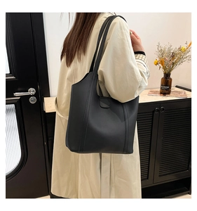 Close-up of minimalist black matte leather tote bag worn with a stylish beige trench coat