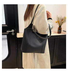 Detail view of large black leather tote bag with wide shoulder strap worn by a model
