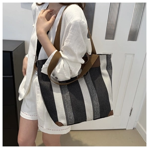Close-up of black and white striped canvas tote bag with brown leather reinforcement details