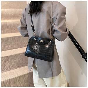 Détail d'un sac à main noir texture crocodile avec fermoir doré porté sur un costume gris