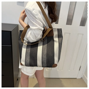 Large striped canvas tote bag with brown leather handles worn by a model in a room