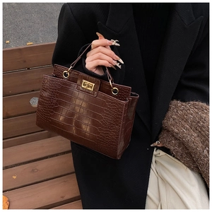 Détail d'un sac à main marron foncé effet crocodile avec fermoir rotatif et anse ronde