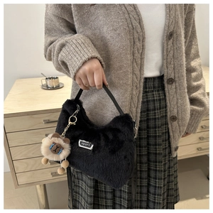 Détail du sac à main en peluche noire avec étiquette argentée et breloque ours brun