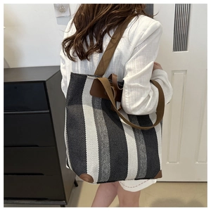 Detail of striped woven tote bag featuring brown leather trim and textile shoulder strap