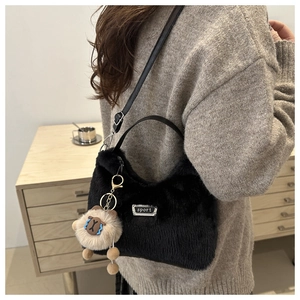 Détail du sac hobo noir en peluche avec plaque sport, lanière en cuir et breloque