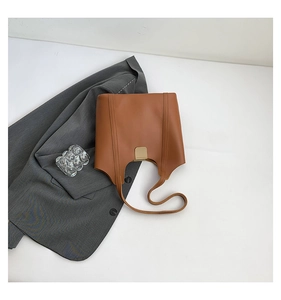 Detail of tan leather tote bag featuring vertical stitching and a gold metallic buckle