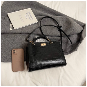 Détail d'un sac à main noir texture crocodile avec fermoir doré posé sur un manteau en laine
