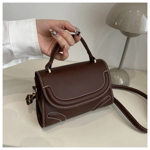 Detail einer braunen Handtasche mit weißen Kontrastnähten und goldener Hardware